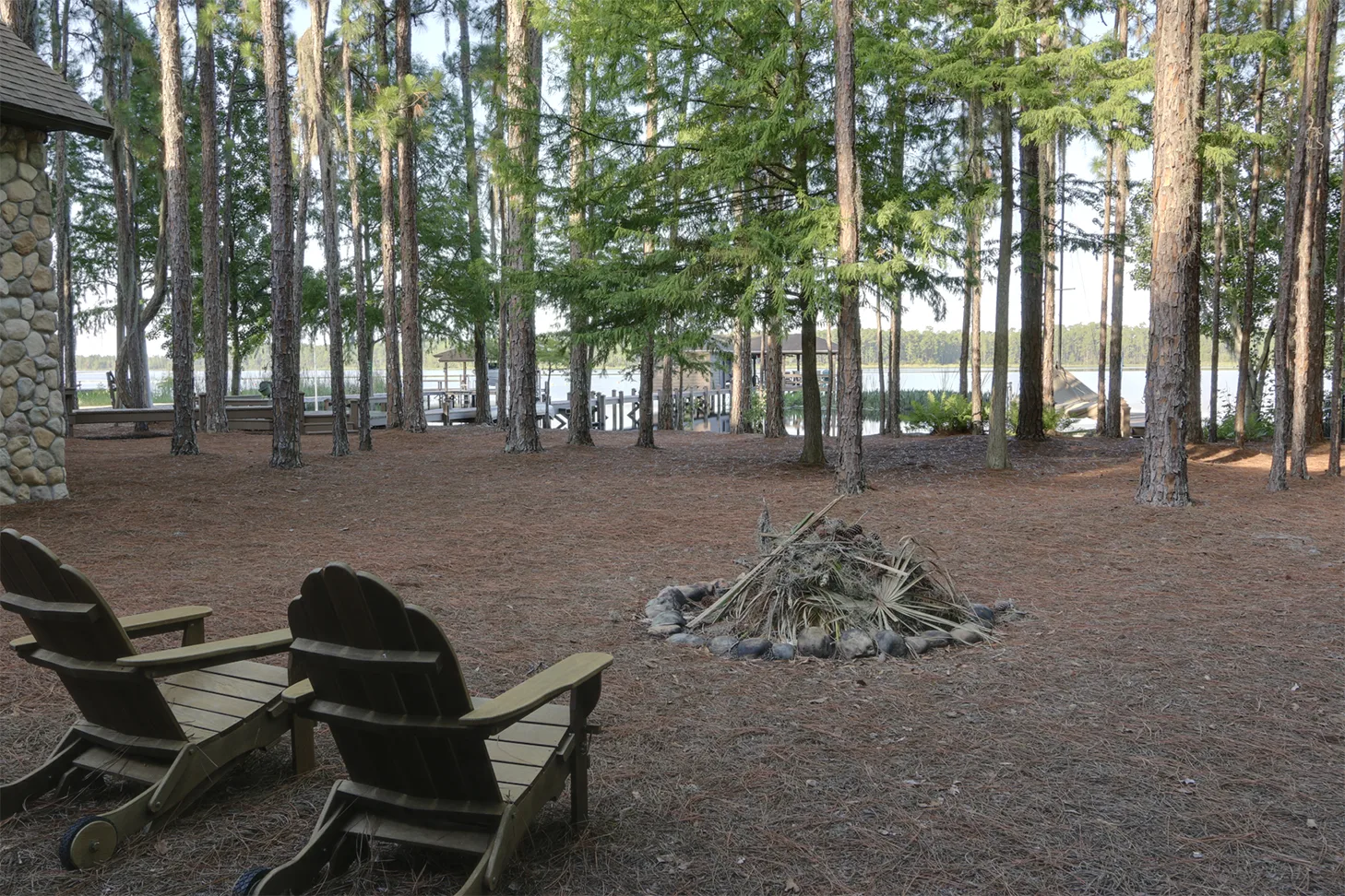 Lakeside chairs and a fire pit beneath shaded trees